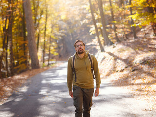 Obraz premium Young handsome man posing in autumn forest. young hipster guy with backpack , traveller standing in woods, Hiking, Forest, Journey, active healthy lifestyle, adventure, vacation concept.