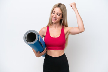 Young sport blonde woman going to yoga classes while holding a mat isolated on white background celebrating a victory