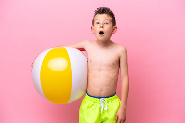 Little caucasian boy holding a beach ball isolated on pink background with surprise and shocked...