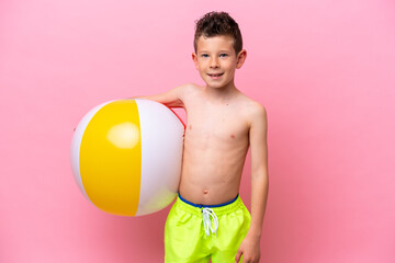 Little caucasian boy holding a beach ball isolated on pink background smiling a lot