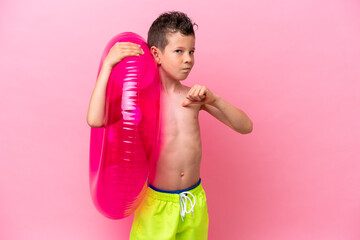 Little caucasian boy holding a inflatable donut isolated on pink background proud and self-satisfied © luismolinero
