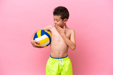 Little caucasian boy playing volleyball isolated on pink background with surprise and shocked...