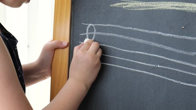 Child drawing a simple treble clef on a chalkboard, violin clef drawn by a child, object detail, closeup, front view. Music, musical symbols, notation and kids musical education abstract concept