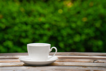 white ceramic coffee mug On the wooden floor, green tree bokeh background.