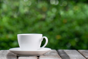 white ceramic coffee mug On the wooden floor, green tree bokeh background.