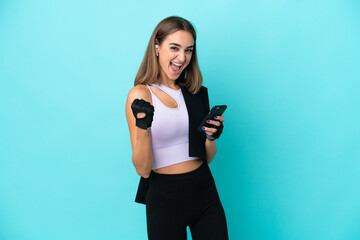 Young sport woman isolated on blue background with phone in victory position