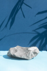 The podium is made of gray stone on a blue background with a shadow from the leaves of a palm tree. Scene for product promotion, beauty, natural eco cosmetic. Showcase, display case.