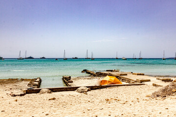 idyllic beach with stone platform, turquoise water, orange umbrella and boats on the horizon, Mallorca, Playa Es Trench
