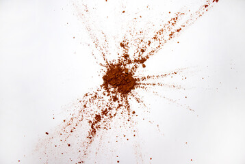 Carob powder on a white sheet of paper. Explosion on the white background above. Carob scattered with a copy of the space