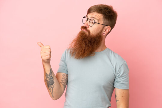 Young reddish caucasian man isolated on pink background unhappy and pointing to the side