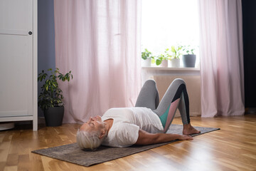 Senior athletic yoga woman doing ardha chakrasana wheel on yoga mat at home