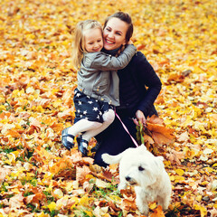 Mother and daughter walking in the park with dog. Happy family enjoying the beautiful autumn nature. Autumn lifestyle, vacation, travel