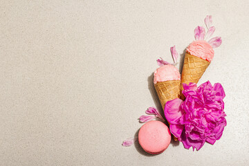 Ice cream waffle cones with macarons on a stone background. Sweet dessert, peonies flower petals