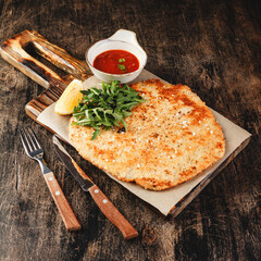 Pork schnitzel with tomato sauce on dark wooden background