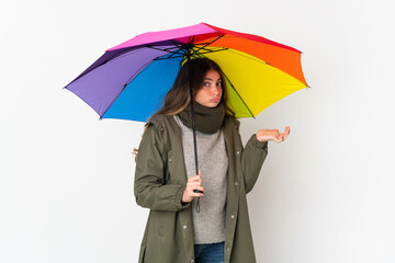 Young caucasian woman holding an umbrella isolated on white background having doubts while raising hands