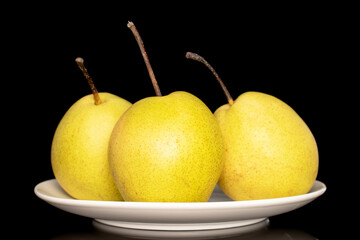 Three organic bright yellow pears on a white ceramic plate, close-up, isolated on a black background.