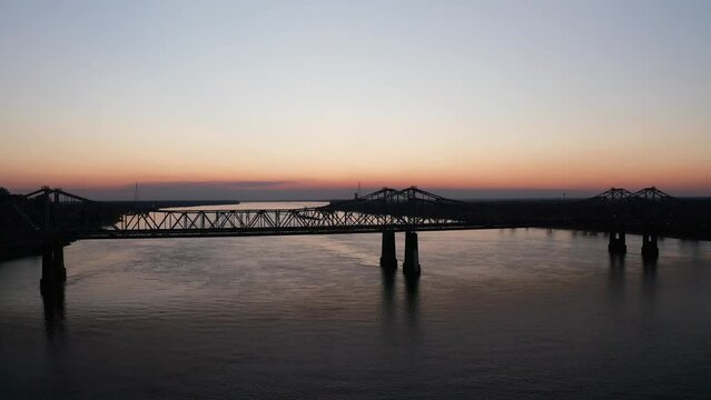 Low aerial shot flying over the Natchez-Vidalia Bridge on the Mississippi River at sunset. 4K