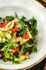 Salad with squid, arugula, celery and avocado, tomatoes and olives on white plate on wooden table