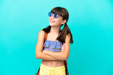 Little caucasian kid going to the beach isolated on blue background looking up while smiling