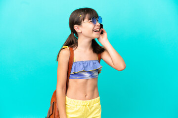 Little caucasian kid going to the beach isolated on blue background keeping a conversation with the mobile phone