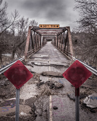 Vertical shot of a broken old road on a bridge with closed red signs