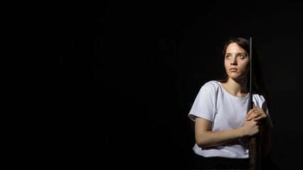 young woman with long hair in a white t-shirt hugging a rifle on a black background with copy space