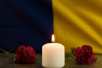 One burning candle against the background of the national flag of Ukraine