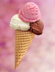 Vanilla, strawberry and chocolate ice cream scoops in wafer cone with pink background