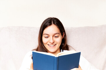 Young woman reading a book and gesturing sitting on the couch at home