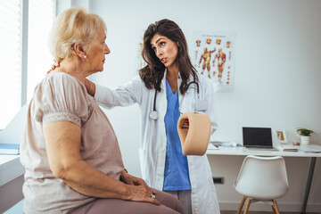 Obraz premium Doctor applying cervical collar on neck of senior woman in clinic. Female doctor putting neck orthopaedic collar on adult injured woman. Woman in pain at the doctor for a neck injury