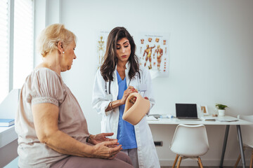 Obraz premium Young woman with injury of neck visiting doctor in clinic. Doctor examining a patient at desk in medical office. Doctor talking to a senior patient with cervical collar at the hospital