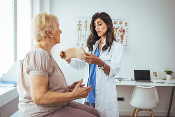 Fototapeta premium Doctor examining a senior female patient's x-ray, she is wearing a cervical collar and having a serious neck injury. Picture of adult woman having a visit at female doctor's office