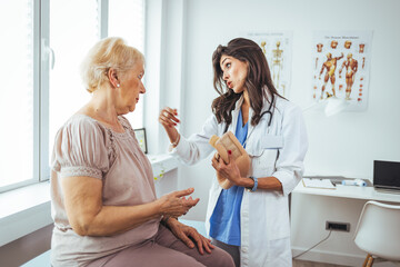 Female doctor putting neck orthopaedic collar on adult injured woman. Doctor talking to a senior patient with cervical collar at the hospital. 