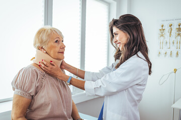 Fototapeta premium Female doctor putting neck orthopaedic collar on adult injured woman. Doctor talking to a senior patient with cervical collar at the hospital. 
