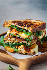 Grilled sandwich with vegetables and mozzarella on wooden board.