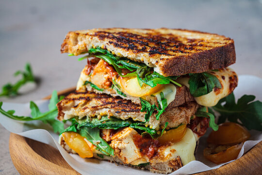 Grilled sandwich with vegetables and mozzarella on wooden board.