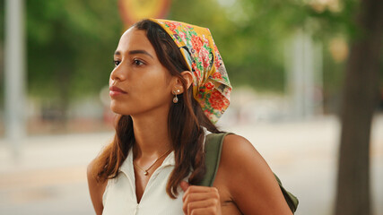 Profile of cute tanned woman with long brown hair in white top and yellow bandana with backpack on...