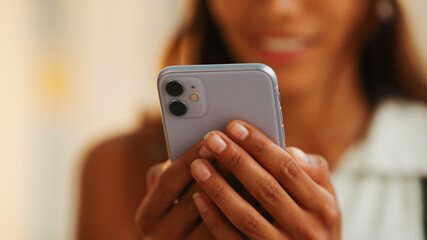 Cute tanned woman with long brown hair wearing white top and yellow bandana with backpack on her shoulder is using mobile phone on modern building background
