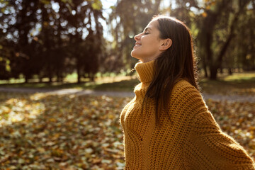 Caucasian woman with eyes closed smiling at the park in autumn - obrazy, fototapety, plakaty