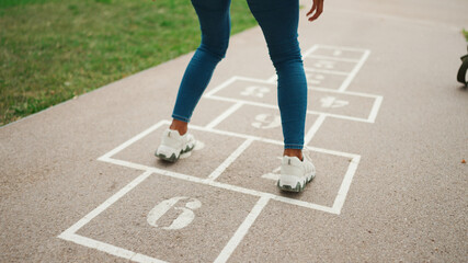 Close-up of young woman hopscotching on city playground. Closeup of the legs of girl jumping on the drawn cells on the pavement