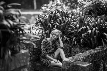 A woman sits on a stone bench in old parkl. Black and white photo.