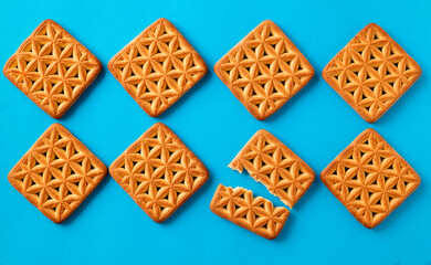 Whole and broken square crackers on a blue background. Top view.