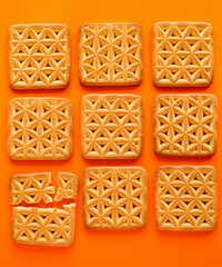 Many square crackers on a orange background. Whole and broken cookies. Top view.