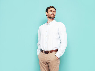 Portrait of handsome confident model. Sexy stylish man dressed in shirt and trousers. Fashion hipster male posing near blue wall in studio. hands in pockets