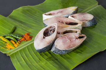 Raw hilsa fish cut into pieces kept on banana leaf for cooking. Shot taken in studio with copy space background and spices.