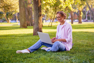 Naklejka na ściany i meble Businesswoman sitting grass summer park using laptop Business person working remote. Outdoor