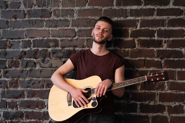 Man with acoustic guitar against brick wall playing music singing songs enjoy life Medium shoot