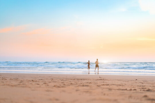 Couple running on the beach. Happy couple go to swim in ocean at sunset. Blurred summer vacation background. Defocused man and woman run on sandy sea beach. Summertime.
