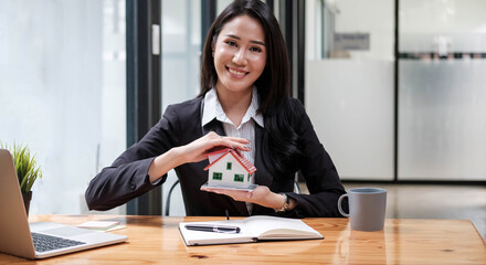 Fototapeta na wymiar Miniature house in the hands of an Asian woman real estate agent home loan working at the office. Looking at the camera.
