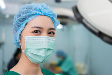 Portrait of Asian woman surgeon with medical mask standing in operation theater at a hospital. Team...
